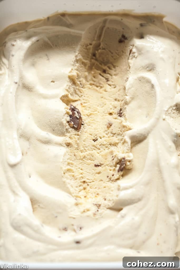 A close-up of the rich, creamy ice cream with a scoop removed, showing its smooth texture and embedded Daim chunks.