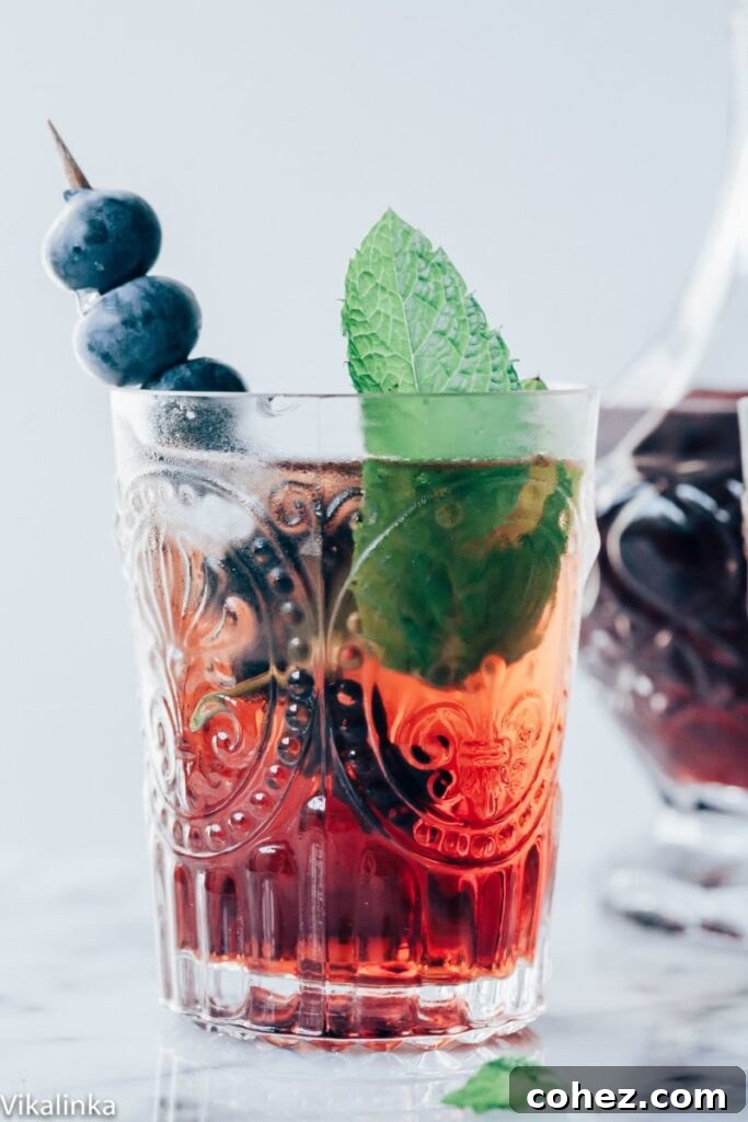 A sparkling Vermouth Cassis cocktail, garnished with blueberries and mint, perfect for a hot day.