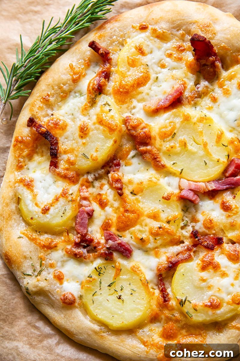 potato and pancetta pizza on parchment paper, with a sprig of fresh rosemary next to it