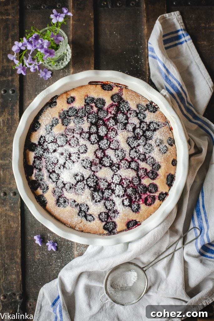 An overhead view of the freshly baked Wild Blackberry Tea Cake, adorned with plump, dark berries glistening on its golden-brown surface, ready to be sliced.