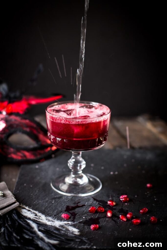 Summer Berry Serenade 4 A vibrant red cocktail glass with ice, garnished with fresh pomegranate seeds scattered around the base, creating a luxurious and inviting scene.
