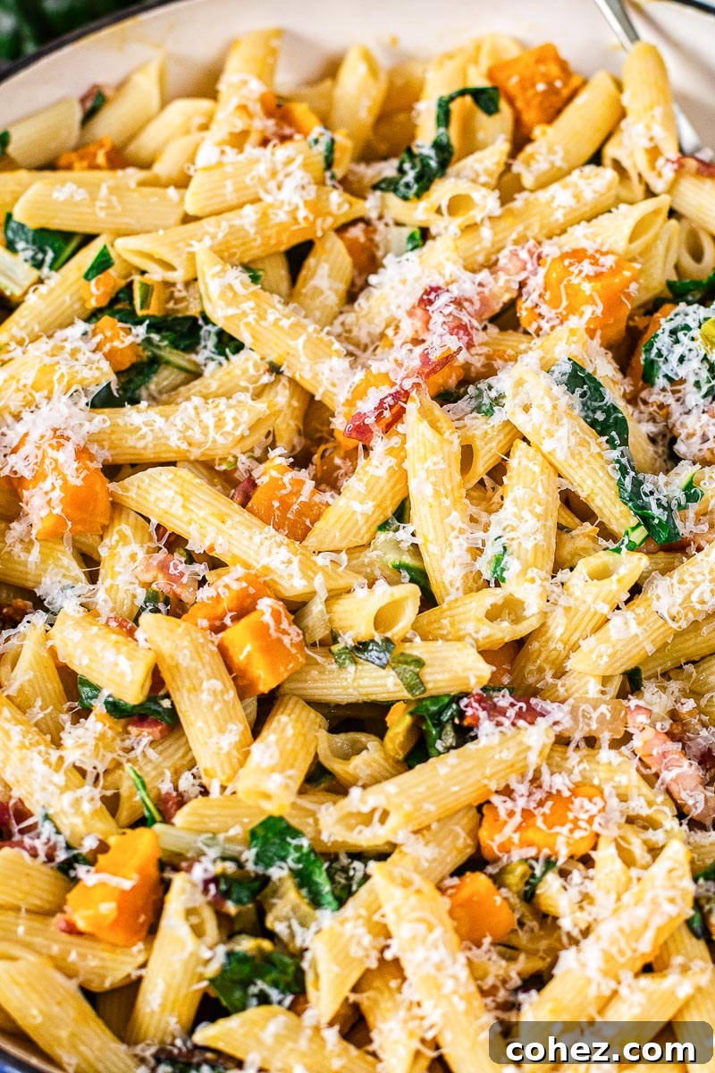 Close-up of penne pasta with roasted squash, golden pancetta, and finely chopped Swiss chard, generously sprinkled with freshly grated Parmesan cheese for a delightful finish.