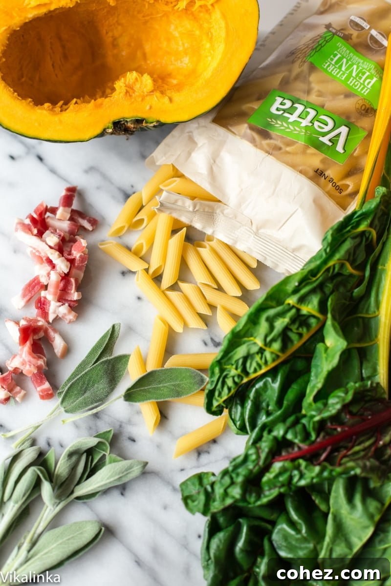 Uncooked penne pasta, vibrant Swiss chard leaves, perfectly cubed roasted squash, and fresh sage sprigs, neatly arranged to showcase the primary ingredients before cooking.