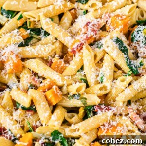 Close-up of penne pasta with roasted squash, crispy pancetta, and finely chopped Swiss chard, generously sprinkled with Parmesan cheese.