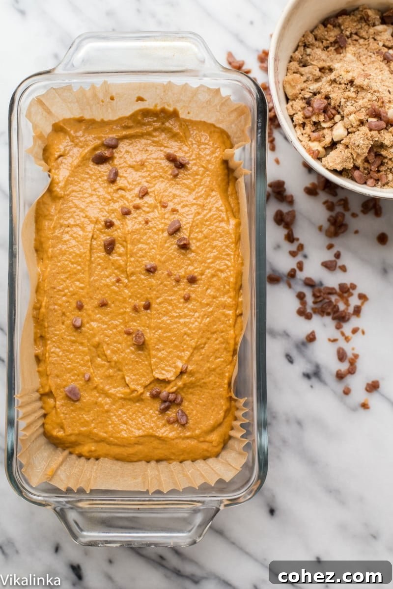 Autumn Spice Pumpkin Loaf with Golden Butterscotch Streusel 3 Fırına girmeye hazır, somun kalıbında çiğ balkabağı ekmeği hamuru, üzerinde zarif bir streusel tabakası görülüyor.