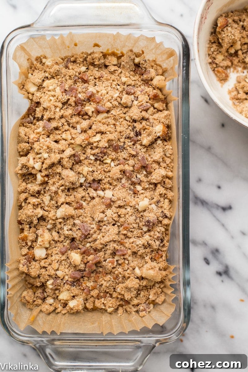Autumn Spice Pumpkin Loaf with Golden Butterscotch Streusel 4 Altın rengi kırıntılar ve erimiş tereyağlı çikolata parçacıklarıyla süslenmiş, tepesi streusel kaplı tatlı ekmeğin bir tavadaki yakın çekimi.