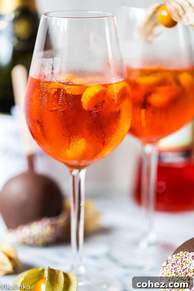 A close-up shot of an Aperol Spritz in a glass, highlighting its vibrant orange hue, ice cubes, and an orange slice garnish.