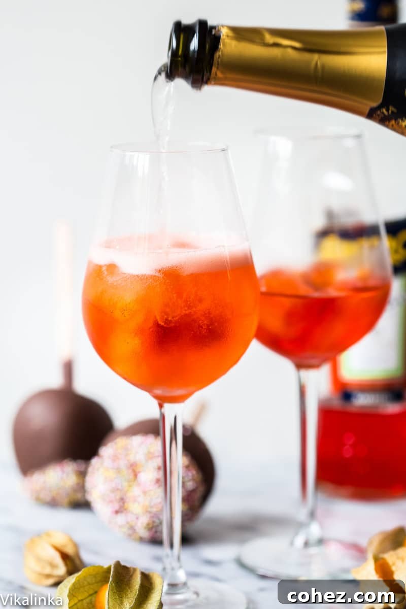 A bottle of sparkling wine being poured into a large glass containing ice and the distinctive orange Aperol drink, creating the refreshing Aperol Spritz.