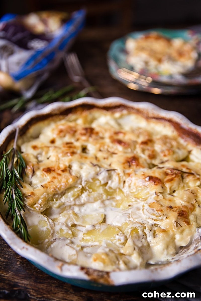 A baking dish of rosemary potatoes au gratin with a spoonful removed, revealing the creamy layers beneath the golden crust