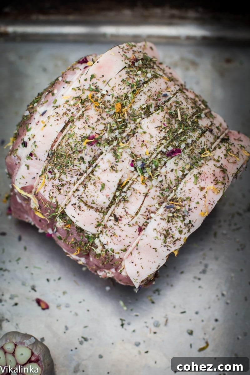 Uncooked pork shoulder roast with a generous rub of herbs and sea salt, ready for roasting.