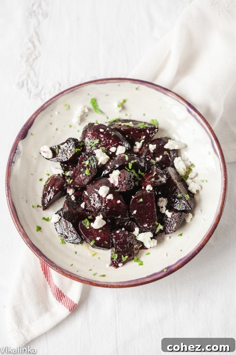 An overhead view of finished balsamic glazed beets, crumbled goat cheese, and fresh mint leaves artfully arranged on a white plate, ready to serve.
