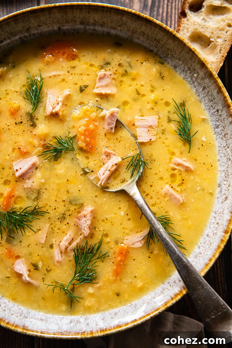 Top down view of a rustic bowl of Yellow Split Pea and Ham Soup with a spoon dipped in, garnished with fresh herbs, ready to be enjoyed.