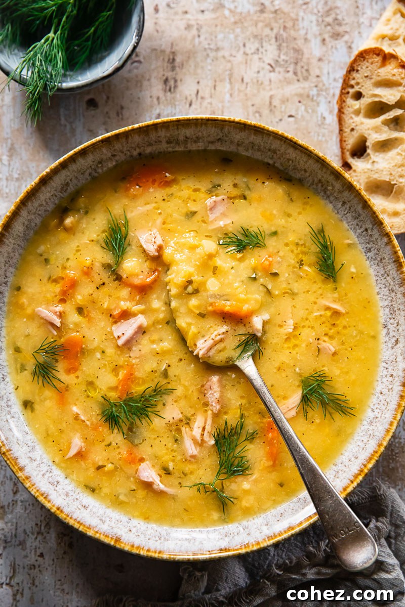 Overhead shot of a bowl of Yellow Split Pea and Ham Soup garnished with fresh dill, accompanied by a slice of rustic bread, inviting a cozy meal.