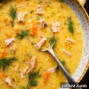 Top down view of a bowl of yellow split pea and ham soup with a spoon in it, ready to serve.