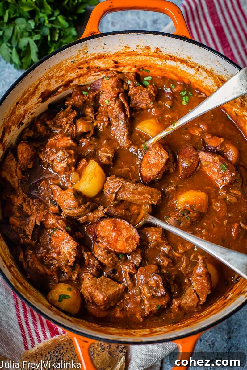 Close-up, top-down view of Solyanka beef and sausage stew bubbling gently in an orange cast iron pot, rich with ingredients.