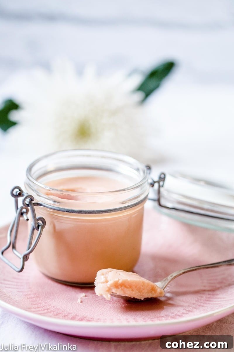 A glistening jar of vibrant homemade rhubarb curd, with a silver spoon scooping a generous portion, showcasing its smooth, creamy texture and inviting pink hue.