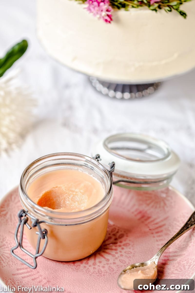 A beautiful glass container overflowing with smooth, vibrant pink rhubarb curd, with a spoonful delicately removed to display its rich, creamy texture, presented elegantly on a white plate.