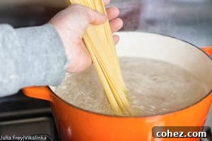 Effortless Cream-Free Carbonara Sauce 8 Hand adding spaghetti to boiling water