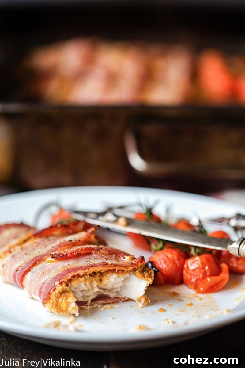 Fish Fillets in Bacon Blankets with Sun-Dried Tomato Pesto 3 Close-up of a perfectly cooked bacon-wrapped white fish fillet with roasted cherry tomatoes, showcasing the golden-brown bacon and juicy fish. An easy and healthy 4-ingredient dinner idea.