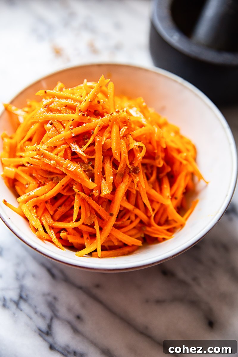 Vibrant Korean Carrot Salad in a white bowl, showcasing julienned carrots and cracked coriander seeds.