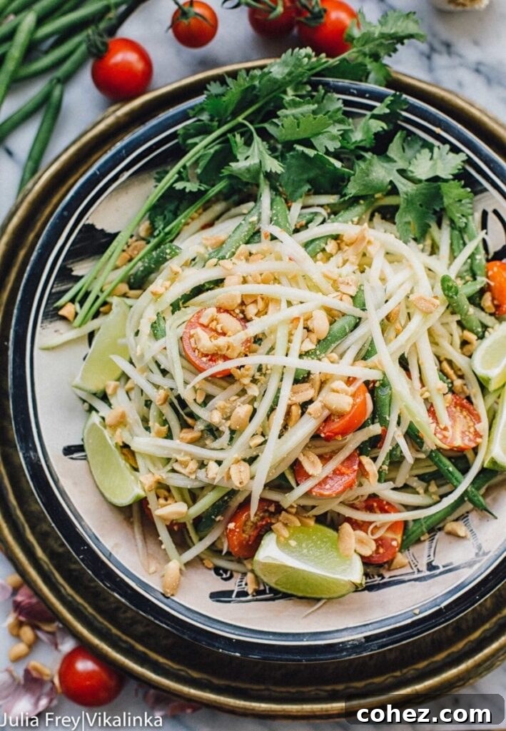 Fiery Som Tam Papaya Salad 2 Top down view of a vibrant Thai green papaya salad in a rustic bowl, garnished with fresh herbs and peanuts.
