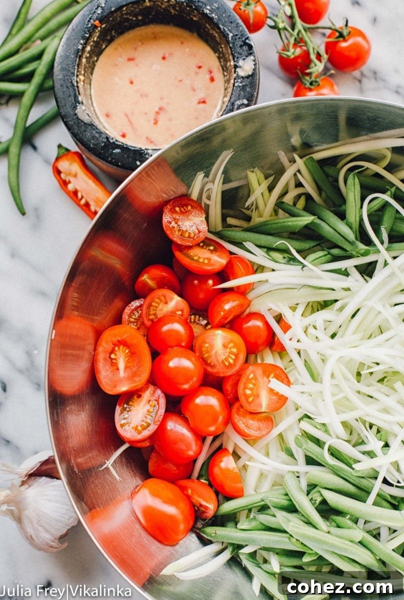 Fiery Som Tam Papaya Salad 4 Close-up of a mixing bowl filled with fresh ingredients like shredded green papaya, halved cherry tomatoes, and crisp green beans, ready for the dressing.
