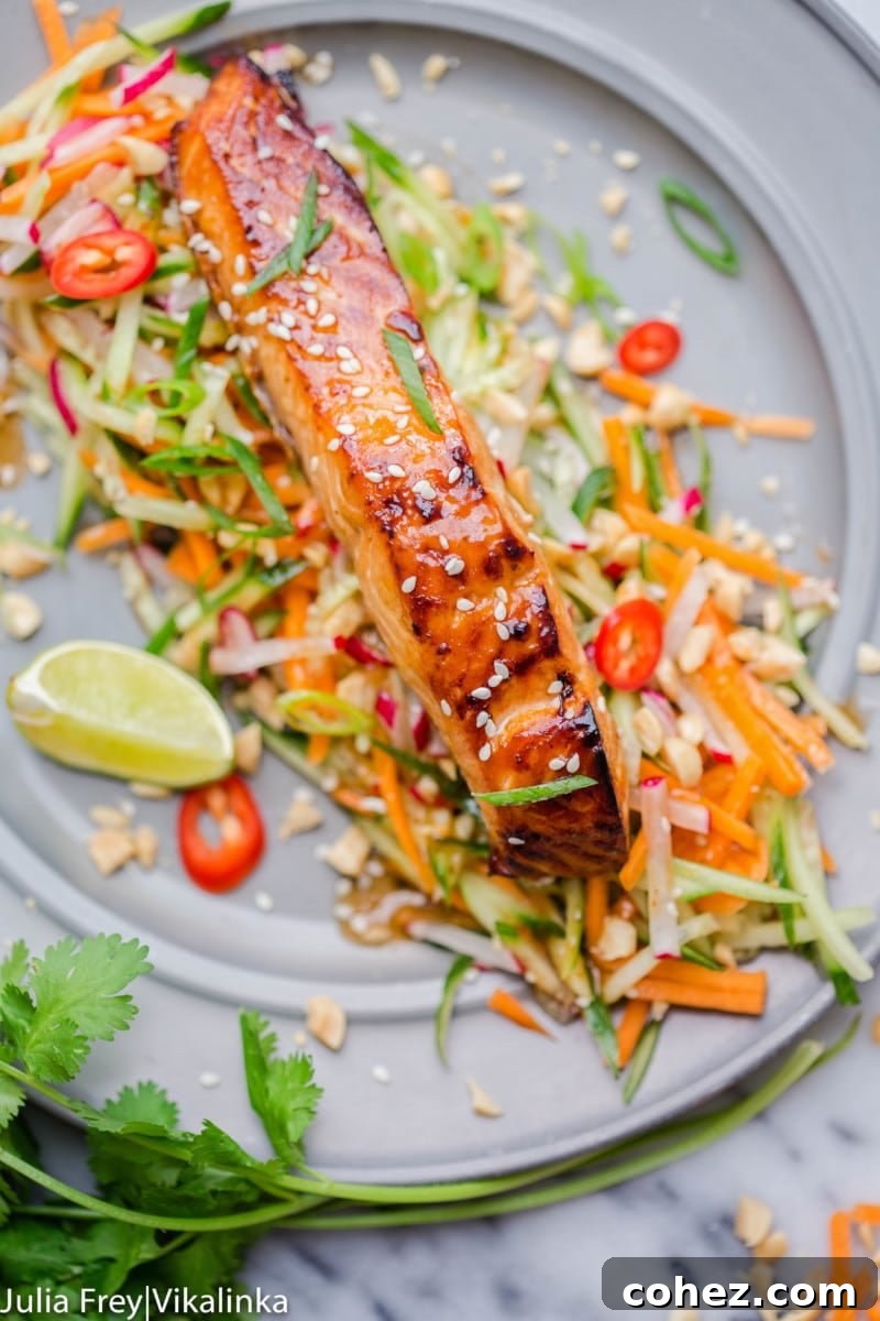 Oven-baked Asian glazed salmon on top of a vibrant carrot and cucumber slaw, garnished with fresh lime wedges and red chillies for a touch of spice and zest.