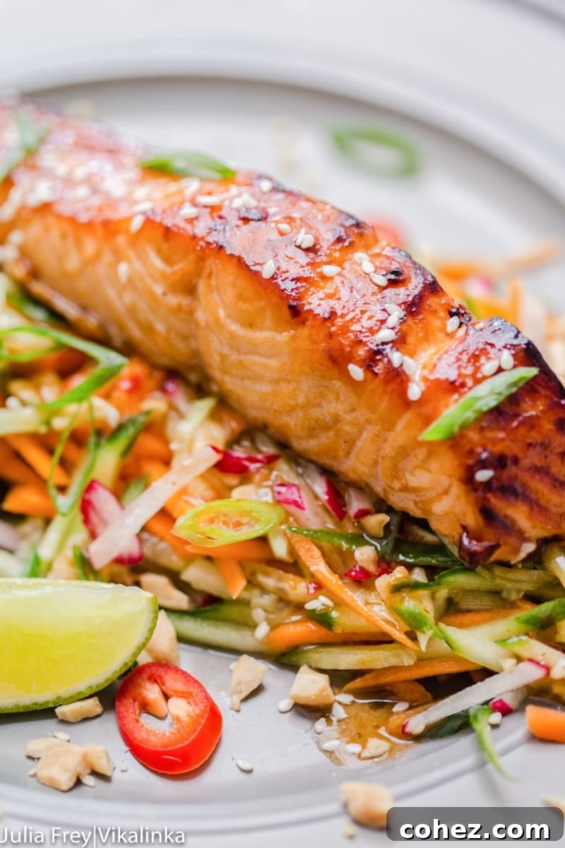 Oven-baked Asian glazed salmon on top of carrot and cucumber slaw, garnished with vibrant red chillies.