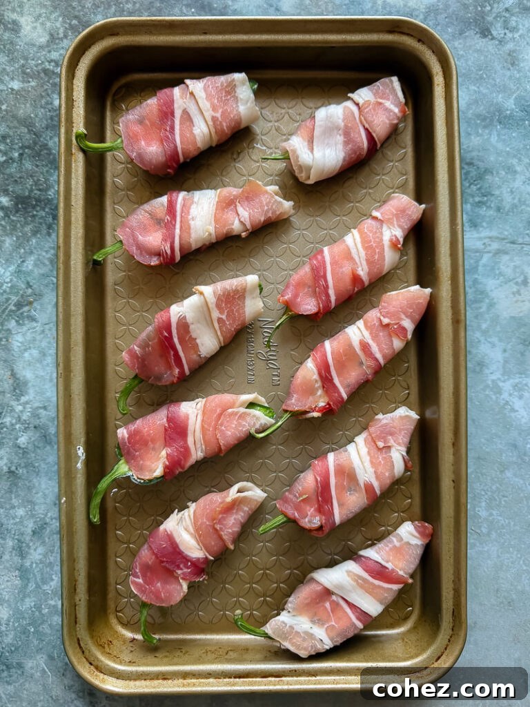 Uncooked bacon-wrapped jalapeño poppers, meticulously arranged on a baking dish, ready for the oven.