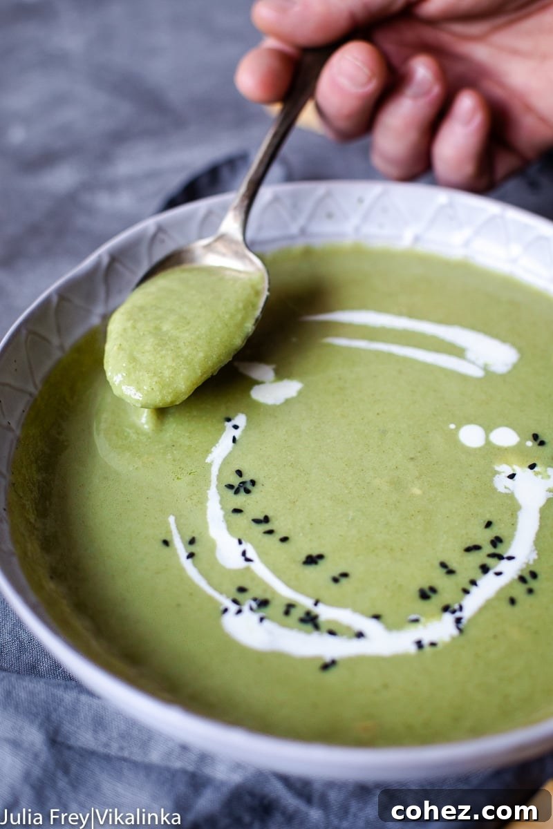 A hand holding a spoon over a bowl of creamy broccoli soup, showing its rich texture and cheesy consistency.