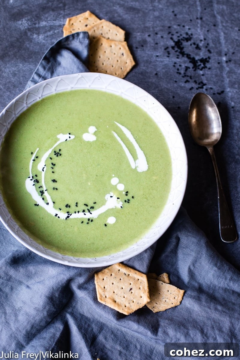 Close-up view of a bowl of creamy broccoli soup, garnished with black nigella seeds and a delicate swirl of cream.