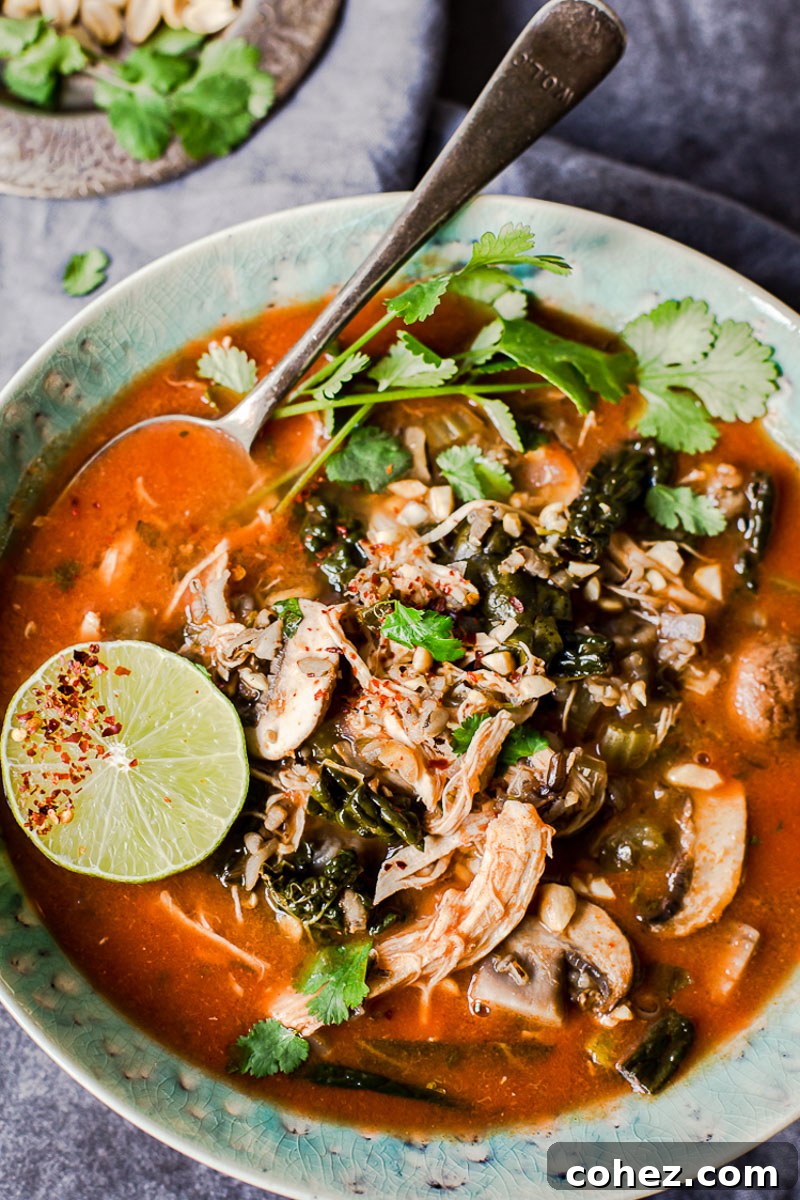 Top-down view of Slow Cooker Thai Chicken and Wild Rice Soup garnished with fresh lime slices and cilantro in a blue bowl