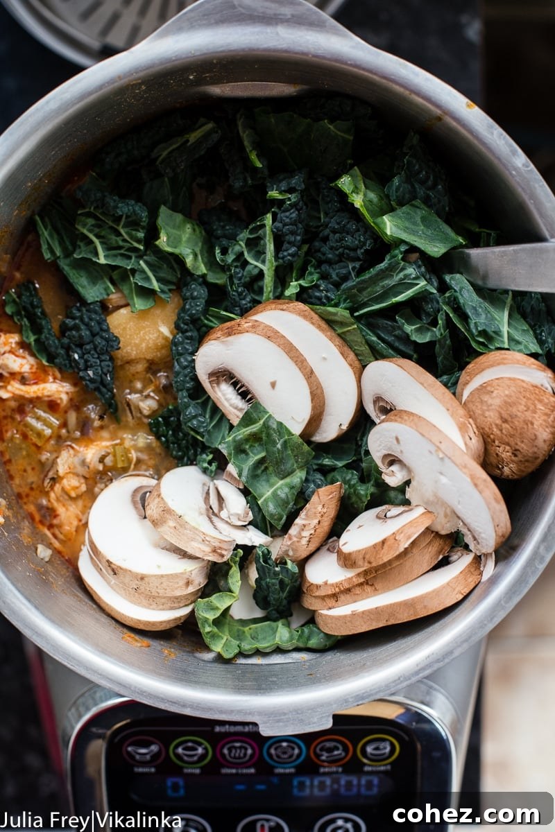 Close-up of sliced mushrooms and kale being added to a rich chicken soup in a pot