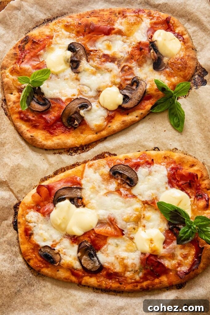 Two baked naan pizzas on a baking sheet, golden and bubbly