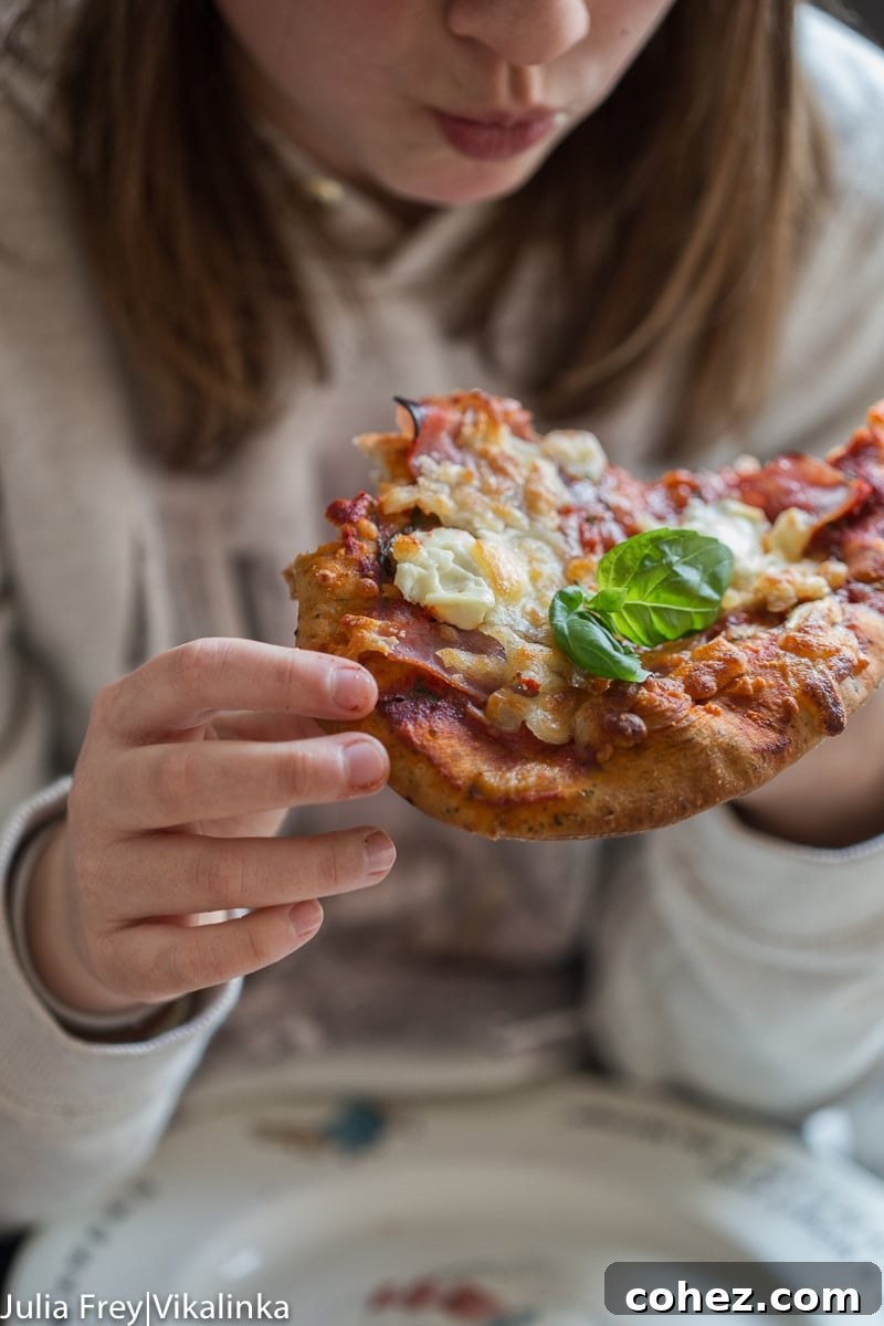 Young girl happily eating a slice of naan pizza, basil clearly visible
