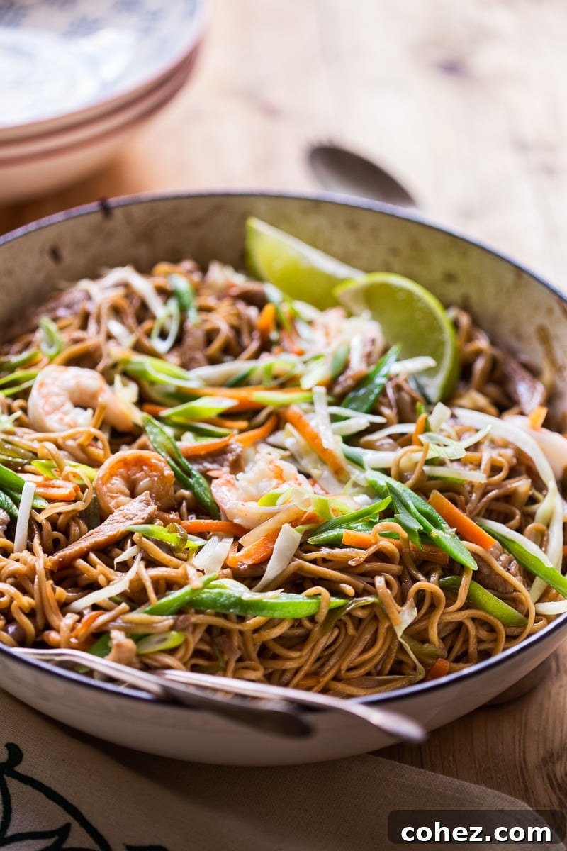 A close-up side view of Pancit Canton cooking in a large pan, showing the rich colors of noodles, shrimp, pork, and vegetables.