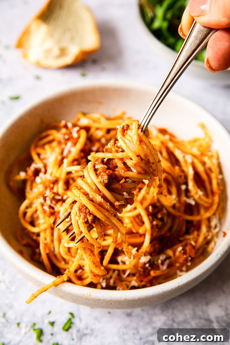 Savory Slow Cooked Bolognese Ragu 4 Spaghetti beautifully twirled around a fork, hovering above a bowl of rich bolognese sauce, inviting a delicious first bite.