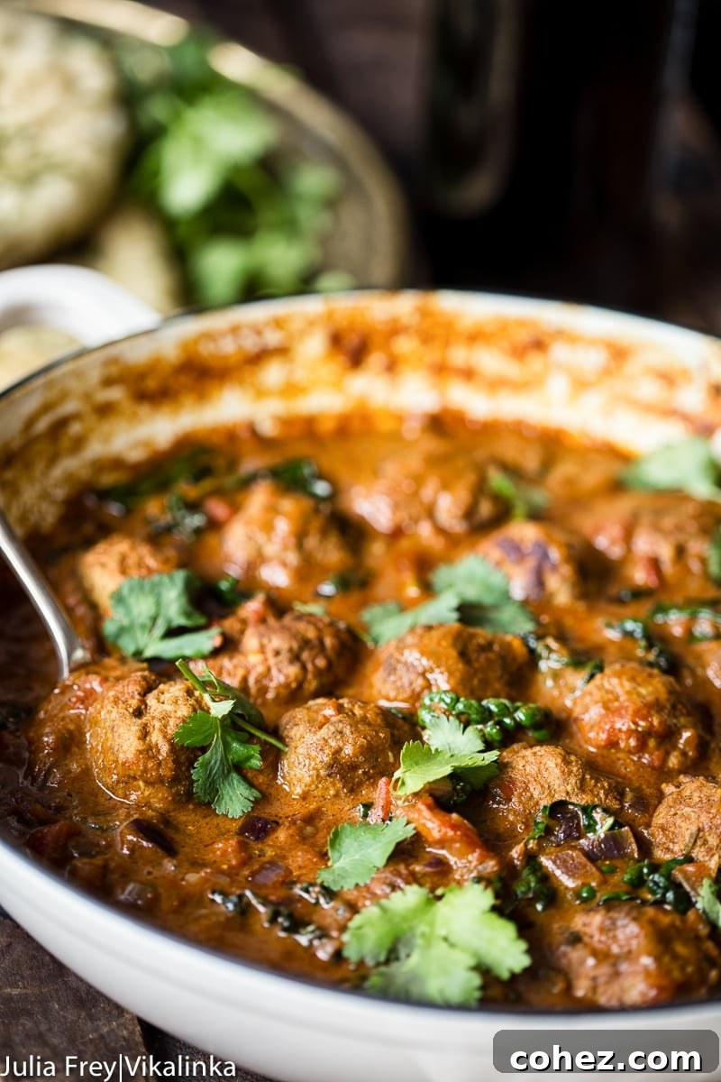 A vibrant Indian meatball curry, also known as kofta curry, topped with fresh cilantro in a white enamel pan, ready to be served.