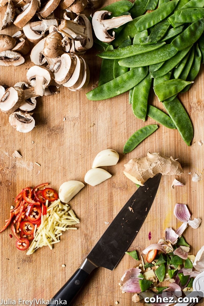 Sliced mushrooms, snow peas, sliced ginger and red chillies, garlic cloves and a knife on cutting board