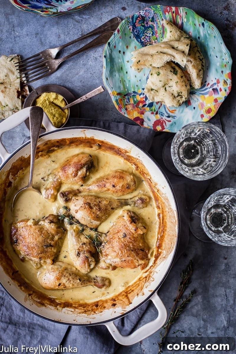 Gourmet Wine and Mustard Chicken 6 Close-up of chicken in a white pan, surrounded by luscious mustard sauce, with two wine glasses and a plate of torn bread pieces on the side