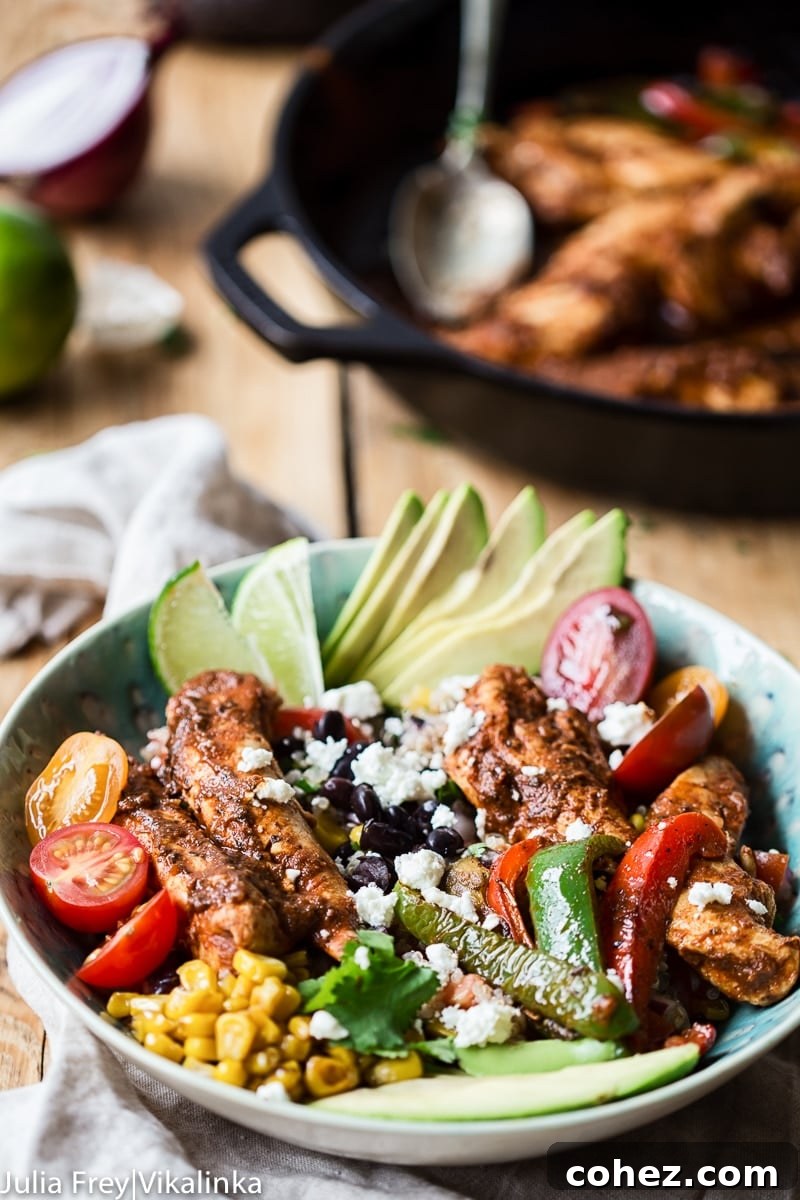 A side view of the Chicken Fajita Bowl, with a pan of cooked chicken and peppers blurred in the background, highlighting the freshness of the assembled dish.