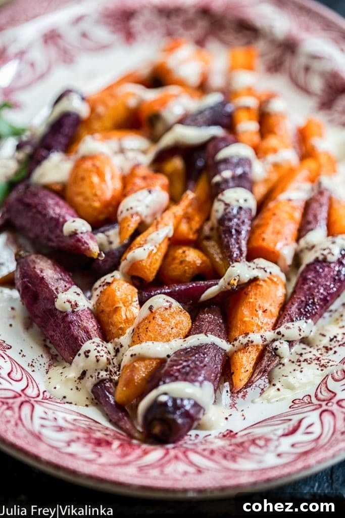 Plate of perfectly roasted carrots drizzled generously with creamy garlicky lemon tahini sauce, garnished with fresh herbs
