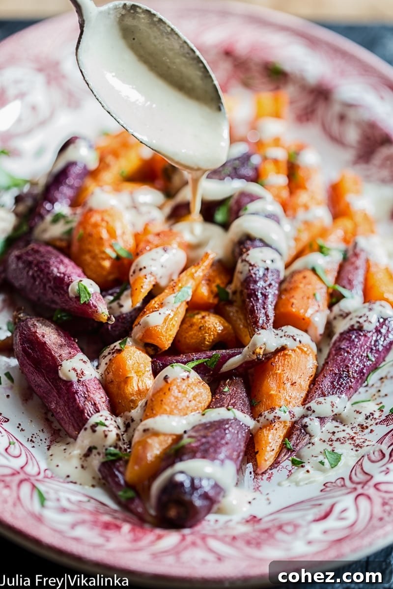 Hand pouring a stream of rich tahini sauce over a platter of beautifully roasted multi-colored carrots