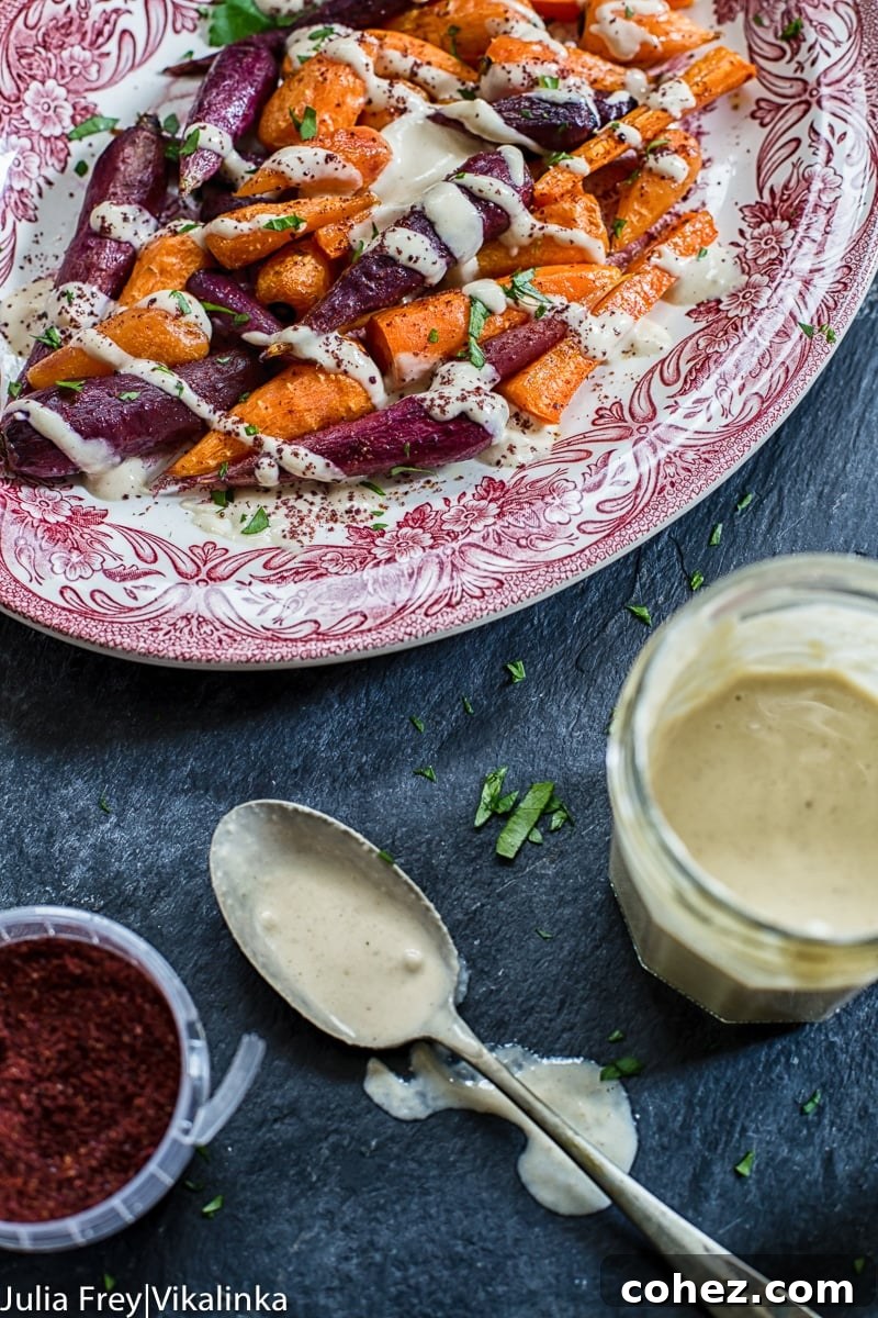 Platter of roasted rainbow carrots served alongside a small jar of garlicky lemon tahini sauce, ready for drizzling