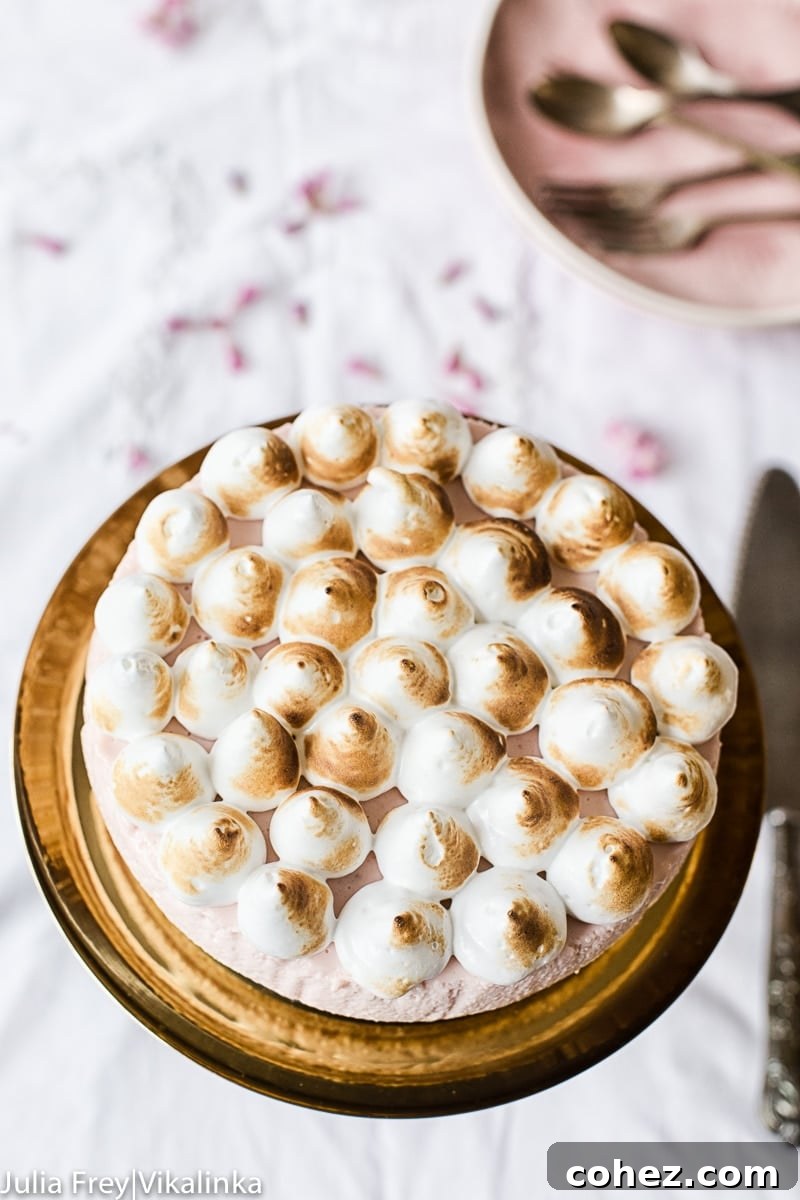 Top-down view of a complete Strawberry Meringue Cheesecake elegantly displayed on a cake stand, surrounded by cutlery, ready to be served.
