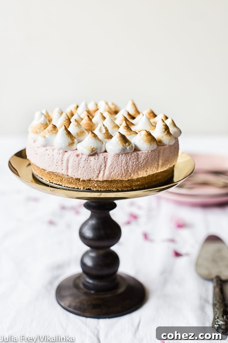 Airy Strawberry Meringue No Bake Cheesecake 5 Strawberry meringue cheesecake on a decorative stand with serving utensils arranged around it