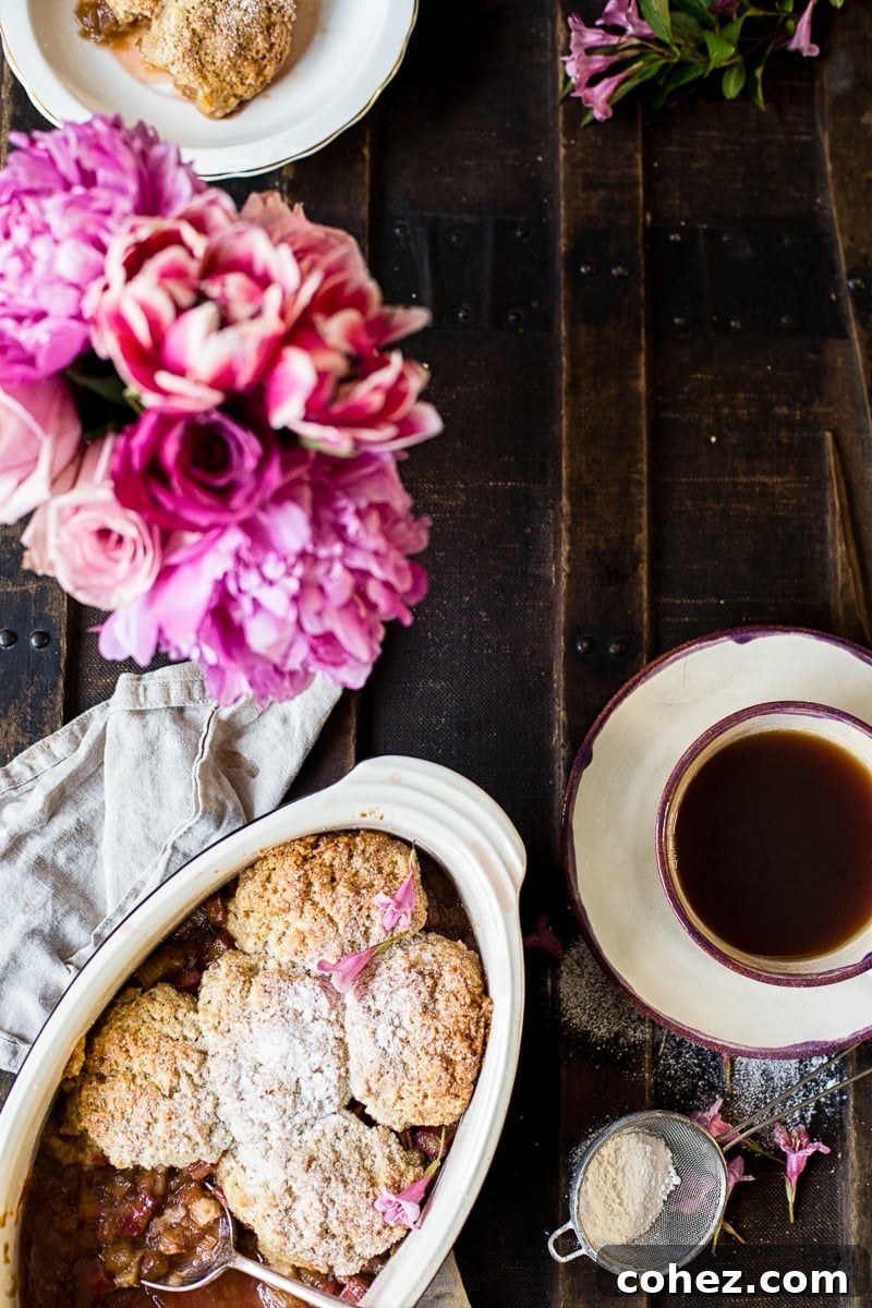 Rhubarb Cobbler from the top down, part of a cozy place setting with tea and flowers, emphasizing its inviting aroma.