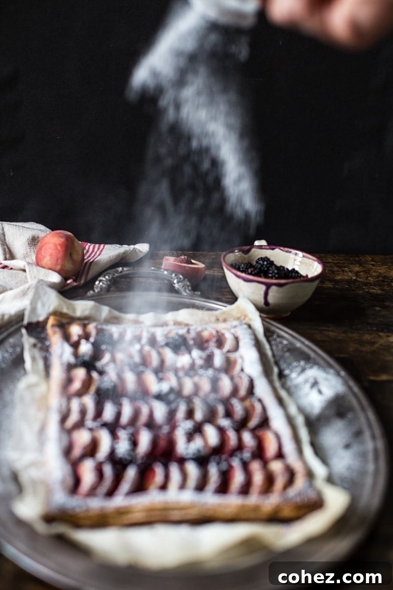 Icing sugar being lightly sprinkled over the baked peach and blackberry tart