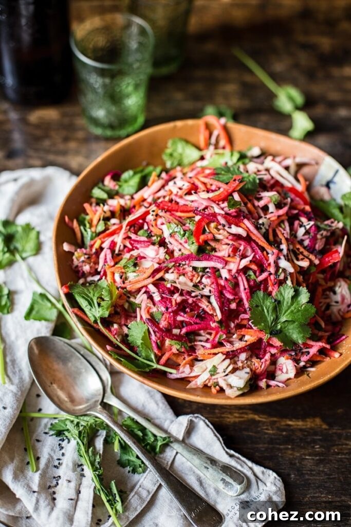Bowl of rainbow slaw on a wooden table, with fresh vegetables in the background.