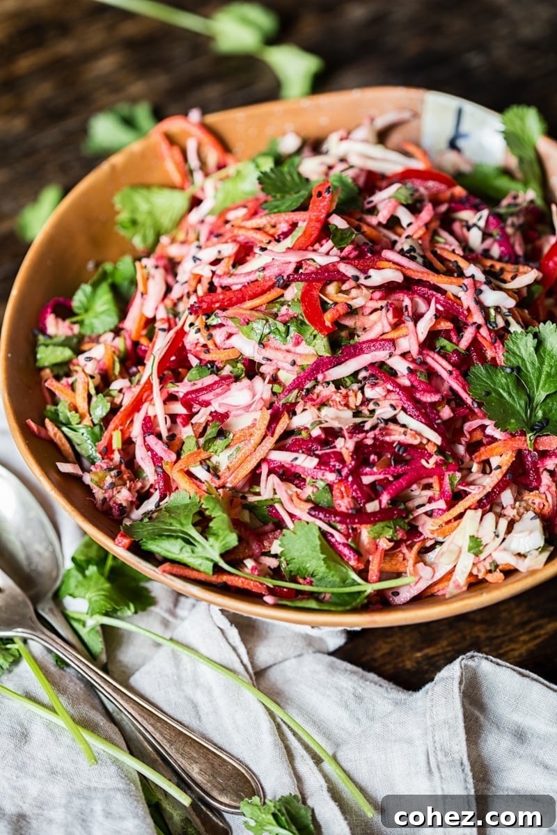 A large bowl of Rainbow Slaw topped with a creamy Lemon Garlic Tahini Dressing and garnished with black sesame seeds.